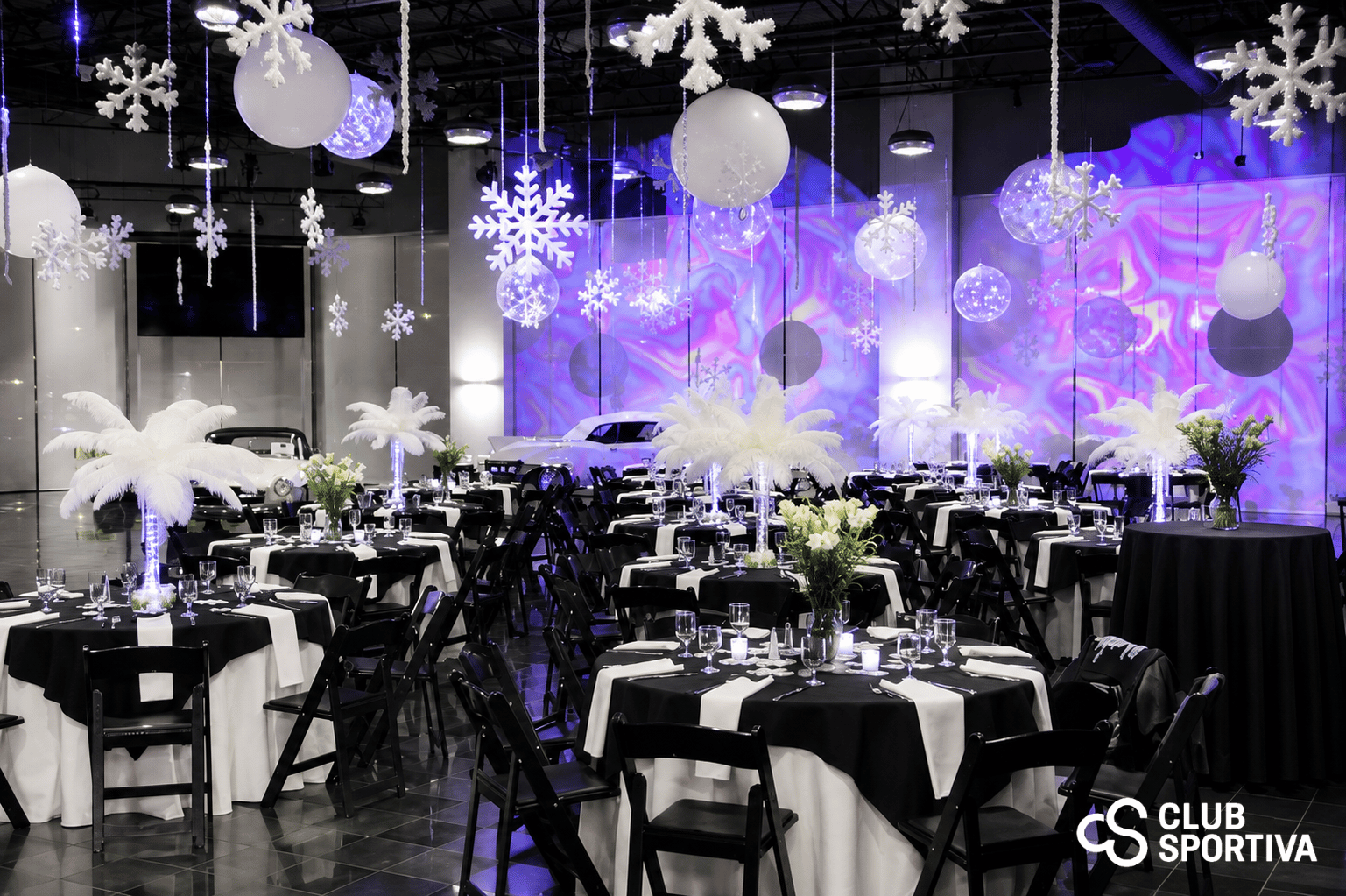 Club Sportiva event venue in San Jose set for a winter-themed gala, with black and white tables, feather centerpieces, hanging snowflakes and classic cars on display.